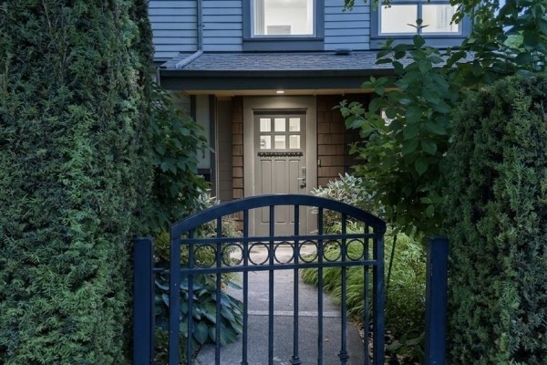 Wrought iron gate opening to pathway leading to townhouse entrance, framed by mature evergreen trees. - 2982 Chesterfield Avenue, North Vancouver