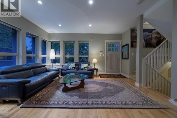 Living room with dark leather sofas, glass coffee table, large Persian rug, and staircase with wooden railing. - 2982 Chesterfield Avenue, North Vancouver