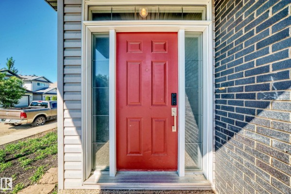 Red front door with glass sidelights and dark grey brick on the exterior. - 2984 Mcphadden Wy Sw, Edmonton