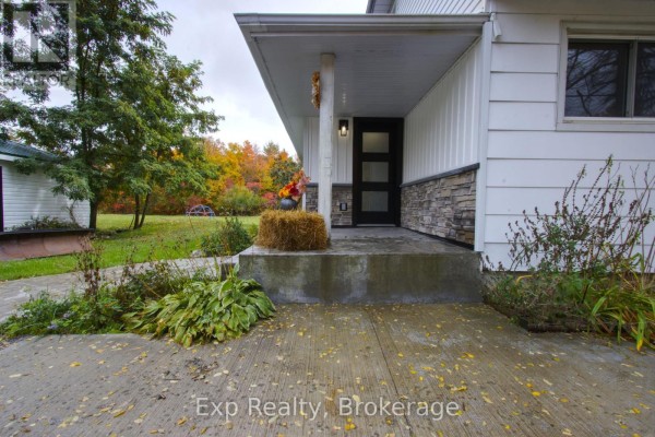 Exterior view of a white house with a covered porch, black front door with glass panels, and autumn foliage. - 2988 County 44 Road, Havelock Belmont Methuen