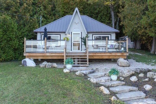 A-frame cottage with grey metal roof, wooden deck, and stone pathway. - 299 Mallory Beach Road, South Bruce Peninsula