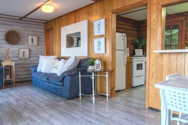 Living room with blue sofa and wood-paneled walls, looking into the kitchen. - 299 Mallory Beach Road, South Bruce Peninsula