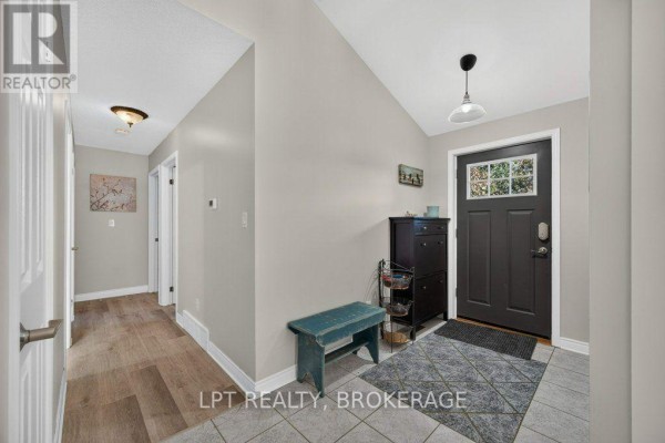 Interior entryway with beige tiled floor, grey walls, a dark front door, and a small bench. - 2994 Campbell Road, Frontenac