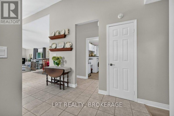 Interior hallway looking towards a living area and a doorway to a kitchen. Light grey walls and tiled floor. - 2994 Campbell Road, Frontenac