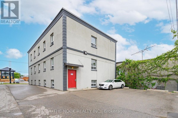 Rear exterior of the commercial building with a red door, a parked white car, and an asphalt lot. - 2b - 337 King Street W, Oshawa