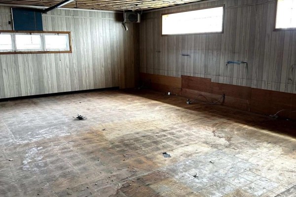 Empty room with wood-paneled walls and two windows, showing a worn floor with scattered debris. - 2nd Floor - 257 Front Street, Belleville