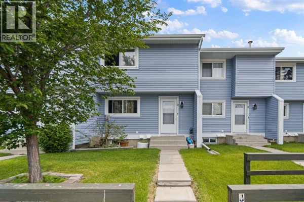 Front exterior of the blue townhouse complex with green lawn and sidewalk. - 3, 195 Manora Place Ne, Calgary
