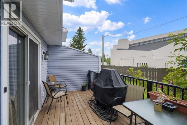 Wooden deck with outdoor furniture and a barbecue next to a sliding glass door. - 3, 195 Manora Place Ne, Calgary