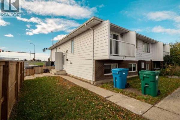Townhouse exterior, showing entrance door, white balcony railing, and windows. Street and cars visible. - 3, 2145 5 Avenue N, Lethbridge
