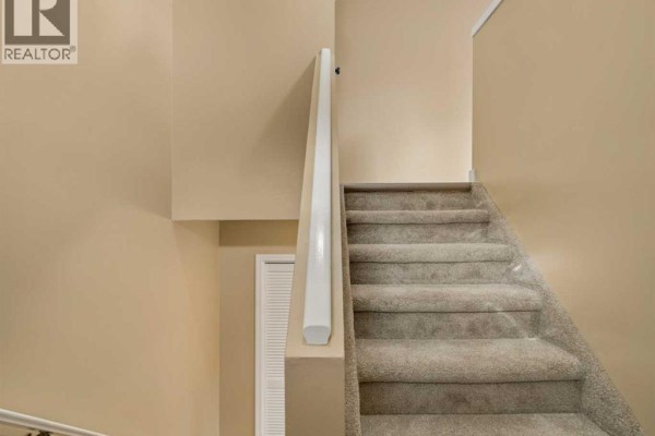 Carpeted stairs leading upwards with a white banister and beige walls. A white door is visible below. - 3, 2145 5 Avenue N, Lethbridge