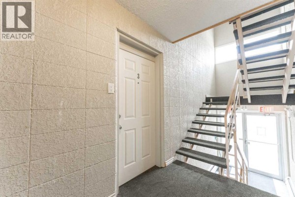 Interior hallway with a white door labeled '3', textured walls, and a metal staircase to the right. - 3, 218 Mayor Magrath Drive N, Lethbridge