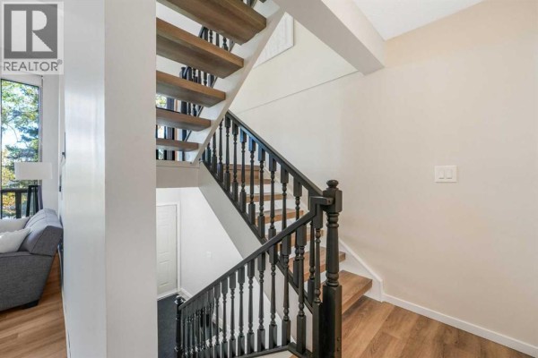 View looking down a staircase with natural wood treads, black spindles, and wood flooring. - 3, 7900 Silver Springs Road Nw, Calgary