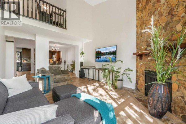 Living room featuring a tall stone fireplace, high ceilings, large windows, and a sectional sofa. - 3, 7900 Silver Springs Road Nw, Calgary