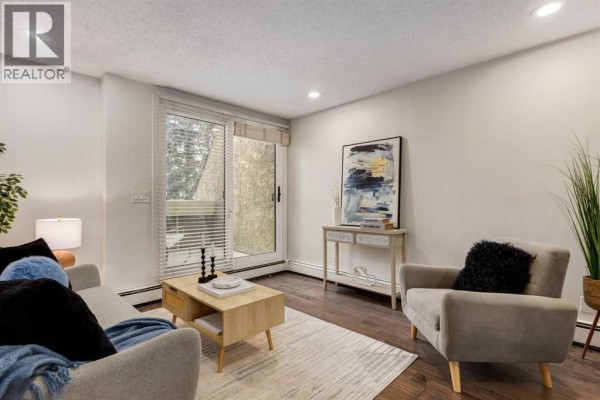 Living room with a gray sofa, armchair, coffee table, rug, and sliding glass door. - 3, 906 4 Avenue Nw, Calgary