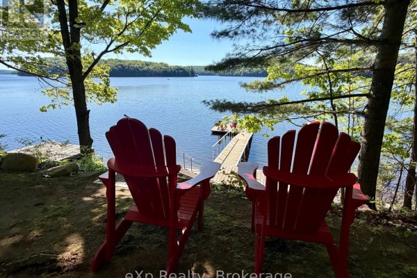 A long wooden dock extends into the dark water, with two red Adirondack chairs at the end. - 3 - 1082 Cowan Park Road, Muskoka Lakes