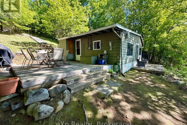The side of a green cottage shows a wooden deck with patio furniture and stairs leading down. - 3 - 1082 Cowan Park Road, Muskoka Lakes