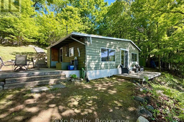 Metal stairs lead down to a wooden dock with two red Adirondack chairs on a serene lake. - 3 - 1082 Cowan Park Road, Muskoka Lakes