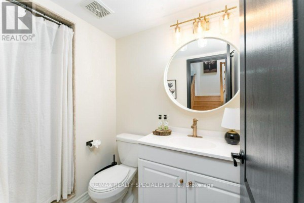Powder room with white vanity, gold faucet, round mirror, toilet, and white shower curtain. - 3 - 1115 Haig Boulevard, Mississauga