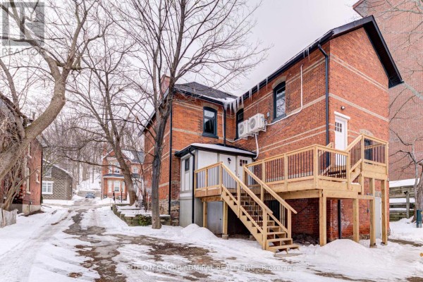 Rear exterior of a brick house with a new wooden deck and stairs, surrounded by snow. - 3 - 167 Collier Street, Barrie