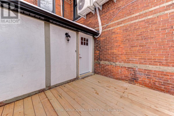 Close-up of a wooden deck with a white door and red brick wall. - 3 - 167 Collier Street, Barrie