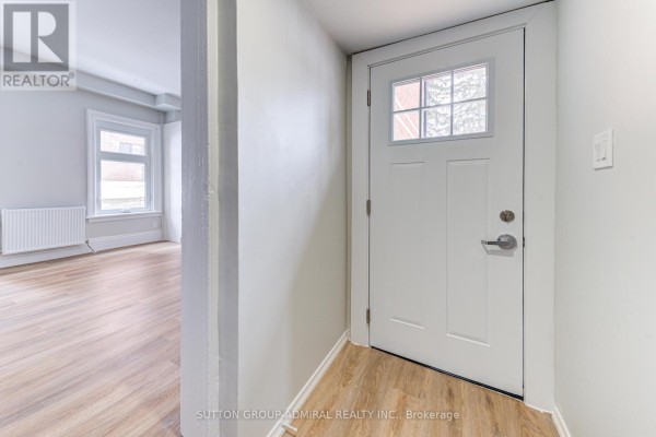 Interior view of a small entryway with a white door and light wood laminate flooring. - 3 - 167 Collier Street, Barrie