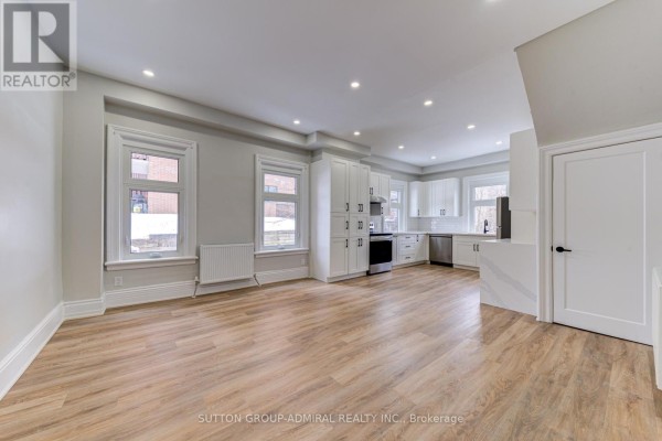 Open-concept living area with light wood floors, white cabinets, and stainless steel appliances. - 3 - 167 Collier Street, Barrie