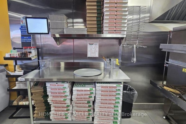 Kitchen prep area with stainless steel tables, pizza boxes, and cooking equipment. - #3 - 17477 Ontario County Hwy 2, Quinte West