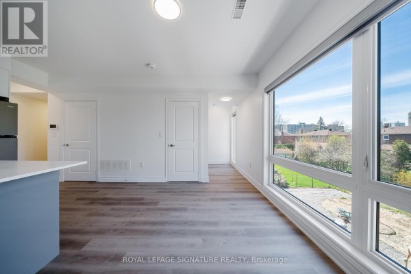 Living area with white walls, grey wood floors, and a large window overlooking the exterior. - 3 - 2052 Pharmacy Avenue, Toronto