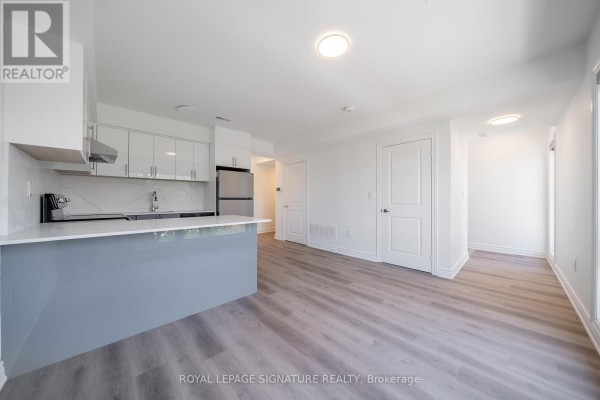 Living area with white walls and doors, grey wood floors, and a large window. - 3 - 2052 Pharmacy Avenue, Toronto