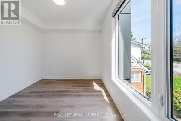 Small room with white walls, grey wood floors, and a large window with an exterior view. - 3 - 2052 Pharmacy Avenue, Toronto