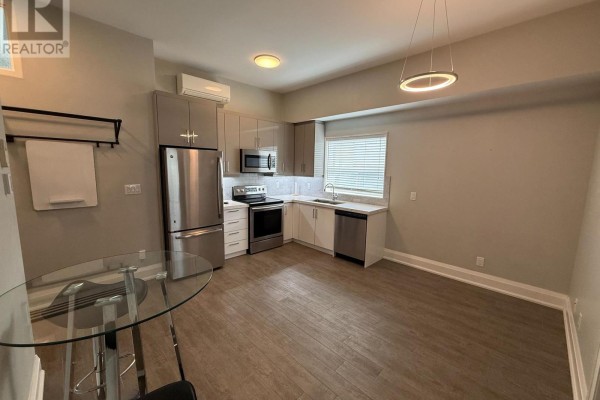 Kitchen with bar stools, glass table, and stainless steel appliances including a refrigerator. - 3 - 2548 Eglinton Avenue W, Toronto