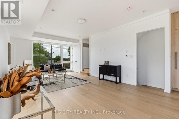Living room with light wood floors, white walls, a black sofa, and large glass doors. - 3 - 276 Lanor Avenue, Toronto