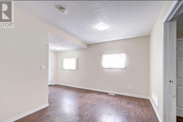Living area with beige walls, dark laminate flooring, and two small windows with white curtains. - 3 - 303 Moffat Street, Orillia