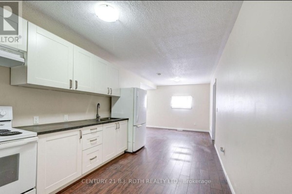 Open concept living and kitchen area with white cabinets, stove, refrigerator, and dark flooring. - 3 - 303 Moffat Street, Orillia