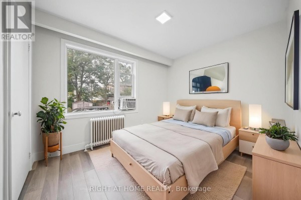 Second bedroom with a queen-size bed, wooden furniture, and a window with a view of brick buildings. - 3 - 32 Vanevery Street, Toronto