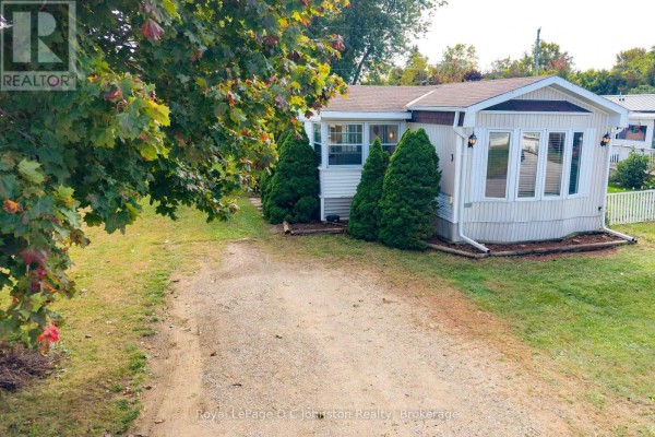 Aerial view of a light beige mobile home with a gravel driveway and mature trees. - 3 - 332 Concession 6, Saugeen Shores