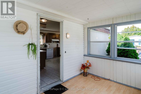 Interior sunroom with white paneled walls, wood-look flooring, and a doorway into the kitchen. - 3 - 332 Concession 6, Saugeen Shores