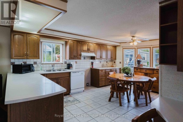 Kitchen with white tiled floor, dark wood cabinets, white countertops, and a wooden dining table. - 3 - 332 Concession 6, Saugeen Shores