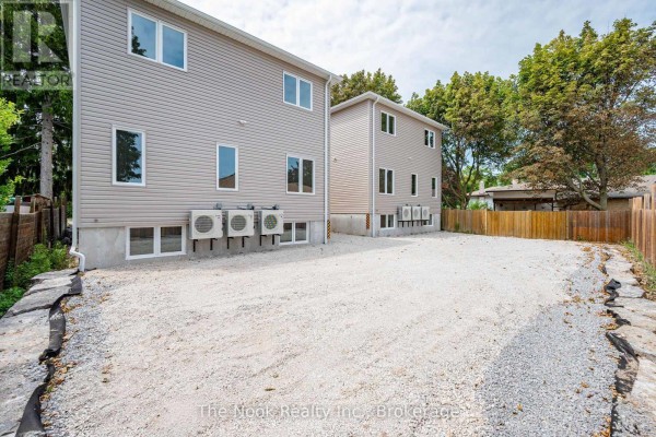 Rear exterior of two townhouses showing beige siding, multiple air conditioning units, and gravel driveway. - 2 - 399 Thorton Road N, Oshawa