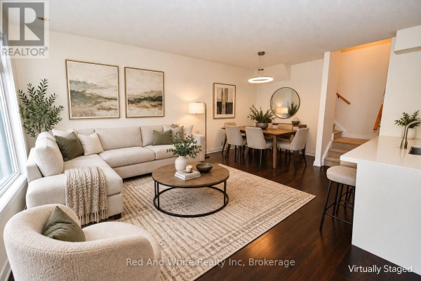 Living and dining area with a blue sofa, massage chair, wooden dining table, and dark wood floors. - 3 - 4080 Parkside Village Drive, Mississauga