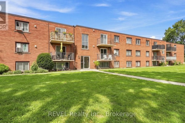 Exterior of a red brick apartment building with balconies and green lawn. - 3 - 450 Carlton Street, St  Catharines