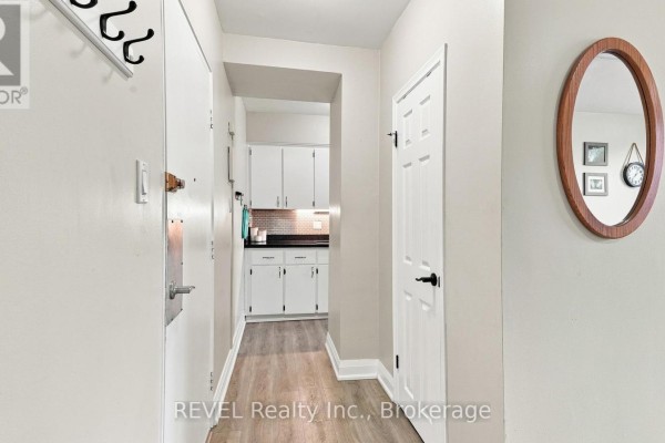 Apartment entrance hallway with light grey walls, wood-look floor, and doorway to kitchen. - 3 - 450 Carlton Street, St  Catharines