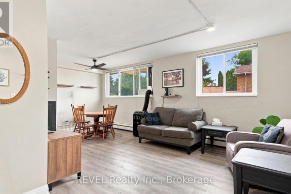 Living and dining area with grey sofas, wooden table, and large windows. - 3 - 450 Carlton Street, St  Catharines