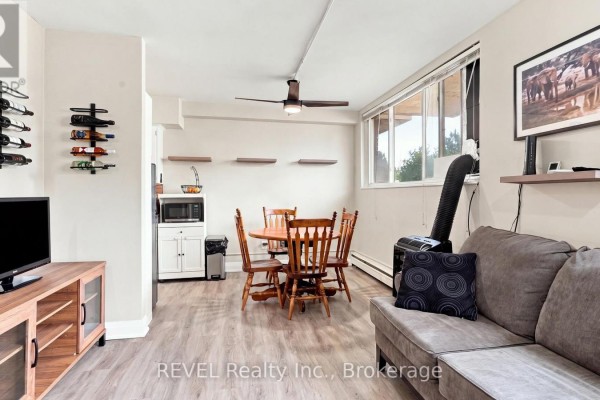 Open concept living space with a kitchen, dining table, and sofas, featuring large windows. - 3 - 450 Carlton Street, St  Catharines