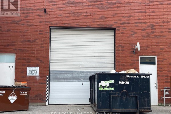 Rear exterior of the commercial building showing a large metal roll-up door and dumpsters. - 3 - 511 Welham Road, Barrie