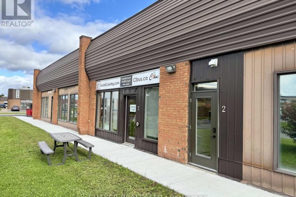 View of the commercial building's exterior, showing multiple storefront units with brick and brown siding. - 3 - 5360 Canotek Road, Ottawa
