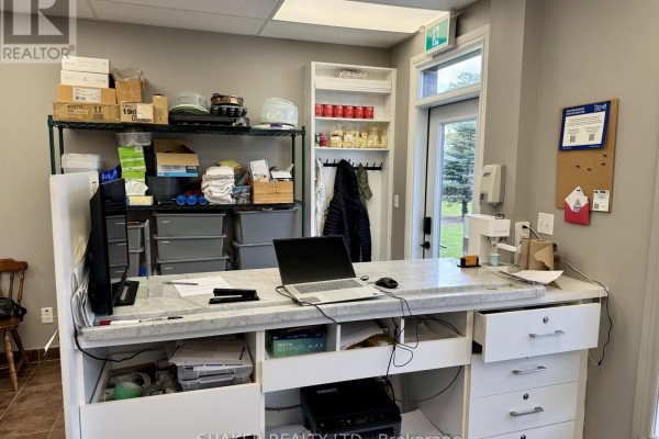 Reception area with a marble counter, laptop, filing drawers, shelving, and a door to the outside. - 3 - 5360 Canotek Road, Ottawa
