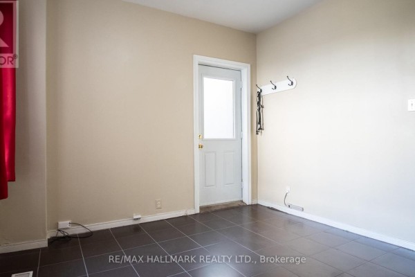A room with a glass-paneled white door and a wall-mounted coat rack, featuring dark tile flooring. - 3 - 560 Jones Avenue, Toronto