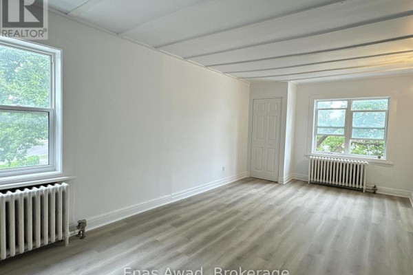 Living room with white walls, white trim, two windows, and a white radiator. - 3 - 64 Genest Street, Ottawa