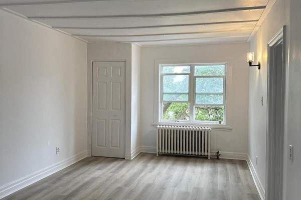 Living room with white walls, a white bi-fold door, two windows, and a white radiator. - 3 - 64 Genest Street, Ottawa